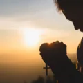 Silhouette of young  human hands praying with a  cross at sunrise, Christian Religion concept background.